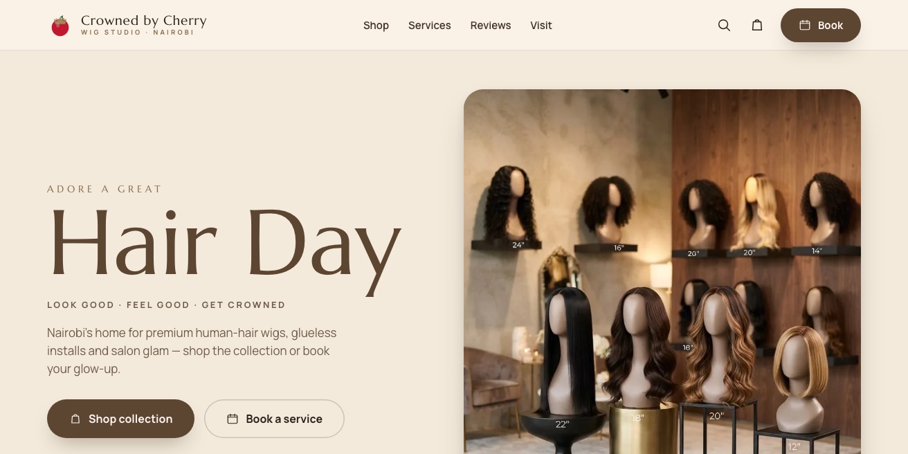 The Crowned by Cherry homepage with the headline Hair Day and buttons to shop the collection or book a service, beside a photo of wigs on display stands in the studio